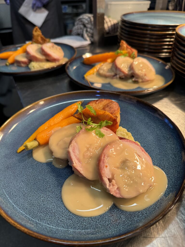 Roasted chicken roulade wrapped in smoky bacon with sage & onion stuffing served with fondant potato, roasted carrots, creamed leeks and a chicken velouté- care catering dish